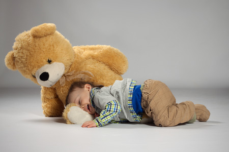 Boy toddler lying and snuggle to a large teddy bearの写真素材