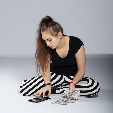 Long-haired teenager girl in striped trousers sitting on the floor and counted dollarsの写真素材