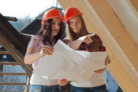Two young women workers standing on under construction roof, and control building in accordance with drawingの写真素材