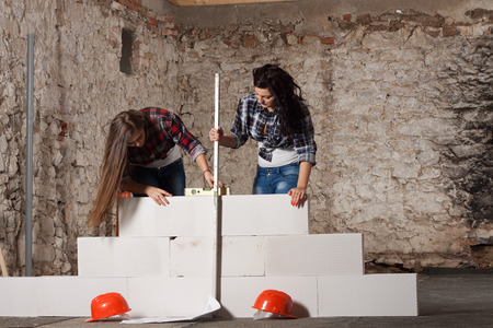 Two young long-haired woman repairing the old house and build a new wall from blocks in accordance with drawingの写真素材