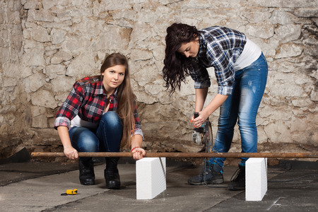 Two young long-haired woman cut iron pipe with angle grinder during the repair an old houseの写真素材