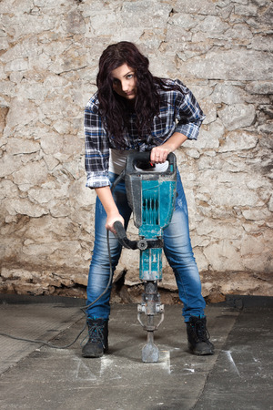 Young long-haired woman working with jackhammer during the repair an old houseの写真素材