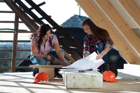 Two young long-haired woman sawed wood for the roof of the house in accordance with drawingの写真素材