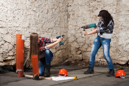 Two young long-haired woman works to repair an old house with an electric drill and cordless screwdriverの写真素材