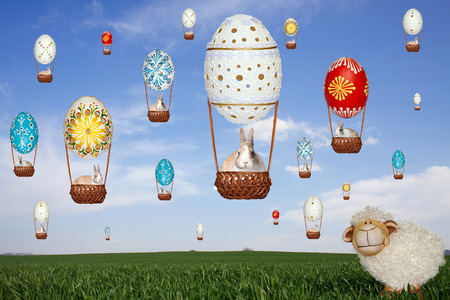 Sheep standing on green grass and monitors balloons from Easter eggs, bunnies flying in balloons on blue skyの写真素材