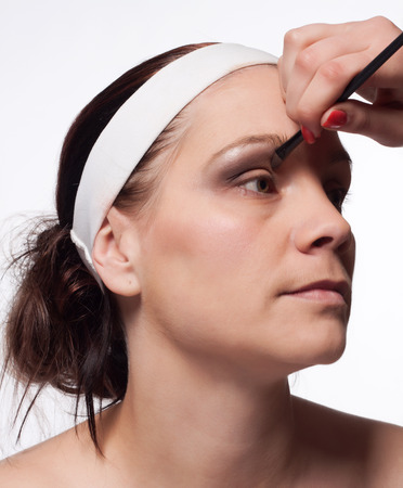 Portrait of young brunette woman with a coronet on her head, with a detail of a hand holding a brush to apply her on the eye brown eyeshadowsの写真素材