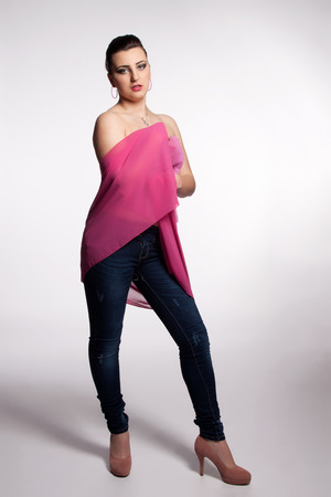 Young woman in pink corset, jeans, high heels with a pink scarf posingの写真素材