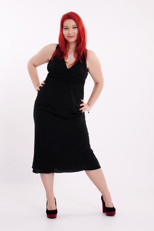 Young plump red-haired woman in black dress posingの写真素材