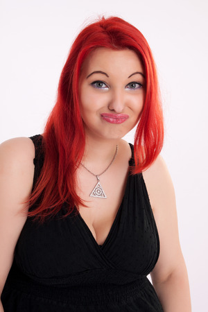 Portrait of young plump red-haired woman in a black dress makes a grimaceの写真素材