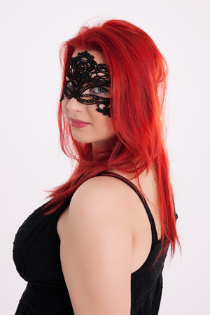 Portrait of young plump red-haired woman with carnival mask on her faceの写真素材