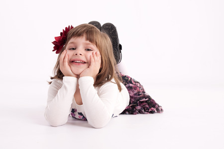 Little girl preschooler model in a flowered skirt with flower in hair lying comfortably on the floor and smilingの写真素材