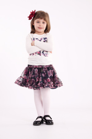 Little girl preschooler model in a flowered skirt with flower in hair posing standing in studioの写真素材