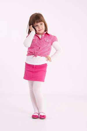 Little girl preschooler model in pink skirt, sandals and dotted shirt and standing with mobile phoneの写真素材
