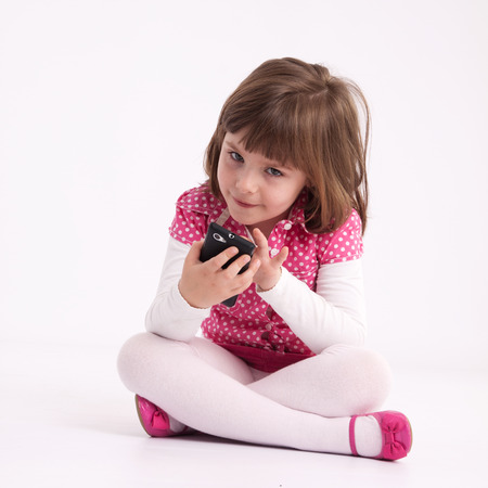 Little girl preschooler model in pink skirt, sandals and dotted shirt and sitting on the floor with mobile phoneの写真素材