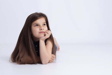 Little preschooler girl in denim shorts and a blue shirt lying on the floor and looks innocentの写真素材