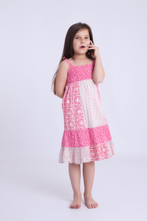 Little preschooler girl in a pink dress holding a mobile phoneの写真素材
