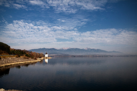 Chapel on the shore of a lake with mountains on the backgroundの写真素材
