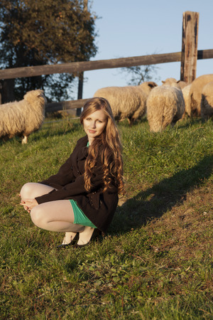 Young long-haired curly blonde woman in a corral with sheepsの写真素材