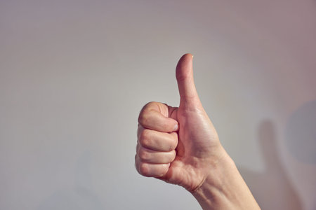 A hand with a thumb up on a light background. Copy space.