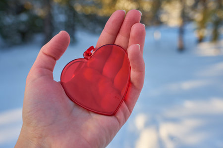 A bright red heart made of glass in the hand against the backdrop of a blurred winter forest. Copy...