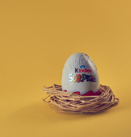 TURKU, FINLAND - FEBRUARY 25, 2021: Kinder Surprise chocolate egg with a toy in a nest on a yellow...