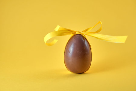 Delicious seasonal chocolate Easter egg with ribbon on a yellow background. Spring concept.の写真素材