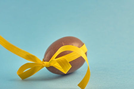 Delicious seasonal chocolate Easter egg with ribbon on a blue background. Spring concept.
