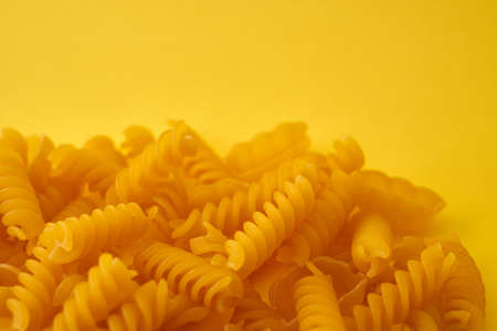Pasta in the form of spirals and shells on a yellow background.の写真素材