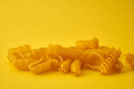 Pasta in the form of spirals and shells on a yellow background.の写真素材
