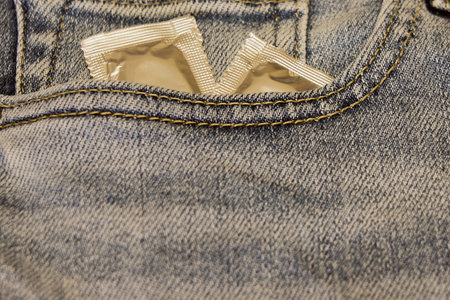 Condoms in silver packaging in the pocket of blue jeans.