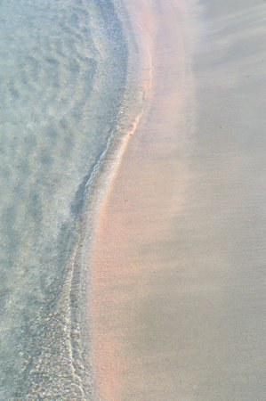 A band of waves snake covers the pink sand, view from above.の写真素材