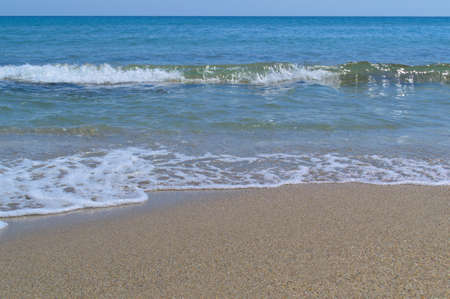 Summer background. Blue sea wave with foam on the sandy shore.の写真素材