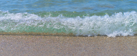 Blue sea wave with foam close-up on the sandy shore.の写真素材