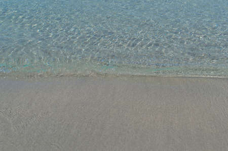 A transparent sea wave covers the sandy beachの写真素材