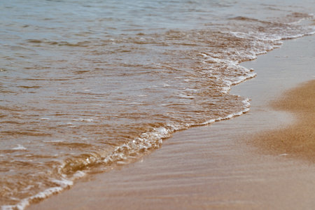 Wave with foam on the sandy beachの写真素材