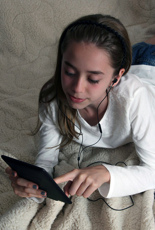 Teenager girl wearing earphone playing on tablet and listening musicの写真素材