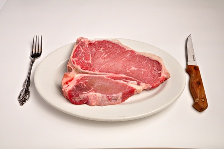 A raw t-bone steak is laying on a white plate on a white background.の写真素材