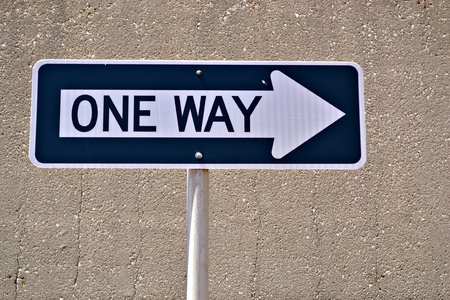 A one way sign with a cement wall as a backgroundの写真素材
