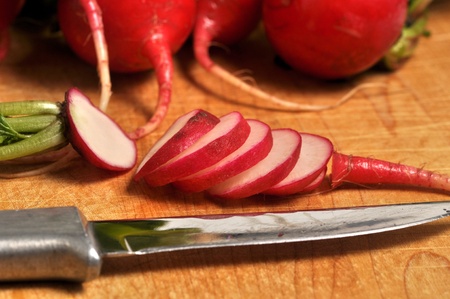 A sliced radish sits on a wooden cutting board with a knife.の写真素材
