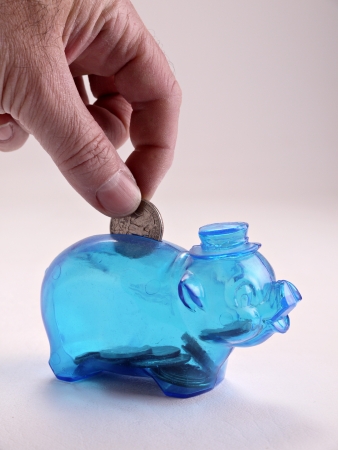 A hand is placing a coin into a childs, blue plastic piggy bank.の写真素材