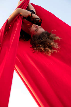 girl acrobat with long hair hanging on red canvasesの写真素材