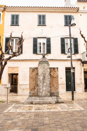 Stone monument with a bust and detailed carvings is located in a charming plaza, framed by historic architecture and trees, reflecting cultural significance and urban beauty.の写真素材
