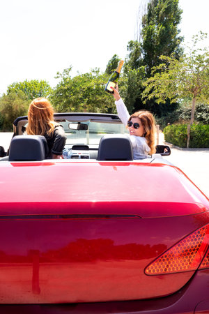 Cheerful girlfriends in a red convertible with a bottle of champagne
