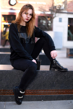 A beautiful red-haired girl, in black clothes, sits with a cup of coffee. Model in black