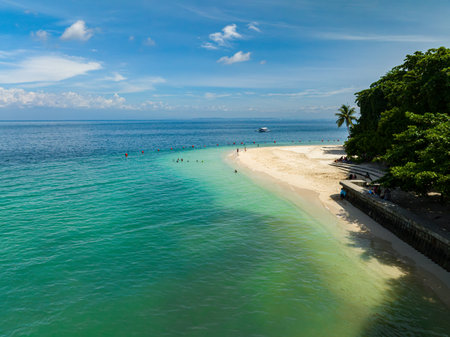 Beautiful sandy beach with waves at coastline. People and boat over the turquoise water. Kaputian Beach. Samal Island. Davao, Philippines.の写真素材