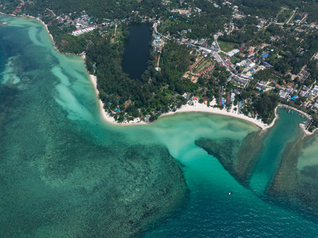 Turquoise sea surrounding lush green coast with scattered buildings and sandy beaches. Ko Pha Ngan, Thailand.の写真素材