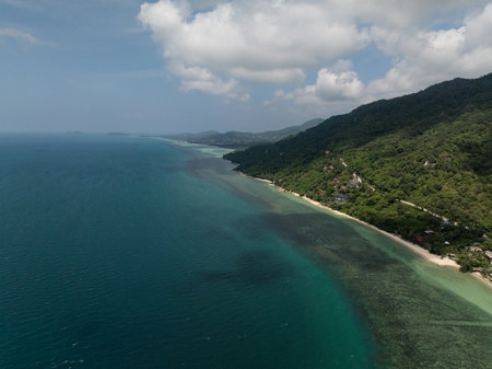 A remote coastline with dense green forest, a winding road, and clear turquoise waters stretching to the horizon. Ko Pha Ngan, Thailand.の写真素材
