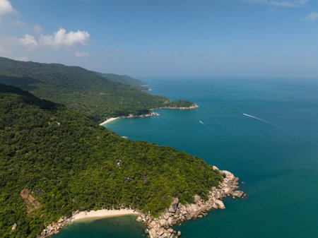 A picturesque coastal village by turquoise waters, surrounded by lush green hills under clear blue skies. Ko Pha Ngan, Thailand.の写真素材