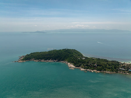 Aerial view of a tropical village with clear turquoise waters and lush greenery on a sunny day. Ko Pha Ngan, Thailand.の写真素材