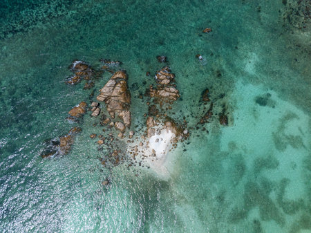 Small rocky islet with clear turquoise waters and coral reefs visible beneath the surface. Ko Pha Ngan, Thailand.の写真素材